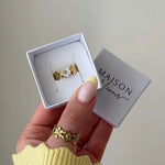 Bague en acier inoxydable dorée à motifs de fleurs et nacre en boîte, une autre bague florale portée au pouce.