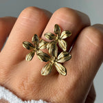 Bague en acier inoxydable doré, 3 fleurs aux pétales striés, portée sur un doigt.