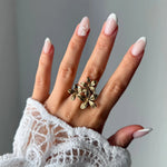Bague ajustable à 3 fleurs en acier inoxydable doré sur une main avec manchette en dentelle.