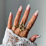 Bague en acier inoxydable doré composée de 3 fleurs, portée sur l'annulaire d'une femme.
