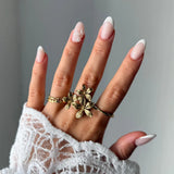Bague en acier inoxydable doré composée de 3 fleurs, portée sur l'annulaire d'une femme.
