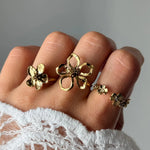 Main avec quatre bagues fleur en acier inoxydable doré. Une grande bague ajourée et une fleur pleine. Deux petites fleurs sur