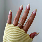 Bague fleur 5 pétales en acier inoxydable doré au doigt, main avec manucure french jaune pastel et pull jaune côtelé.