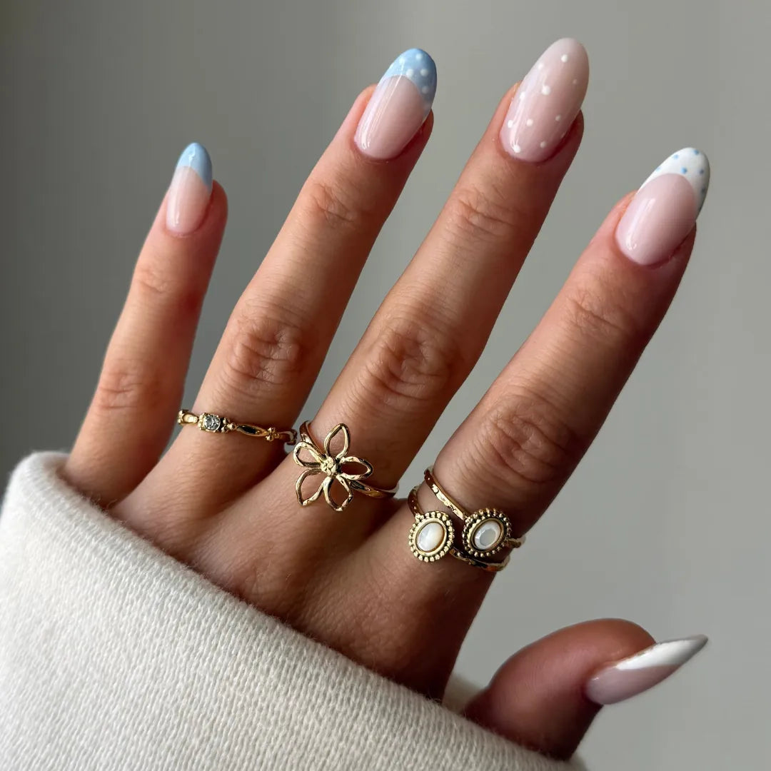 Main portant une bague fleur délicate en acier inoxydable doré effet martelé. D'autres bagues, dont une en nacre, sont