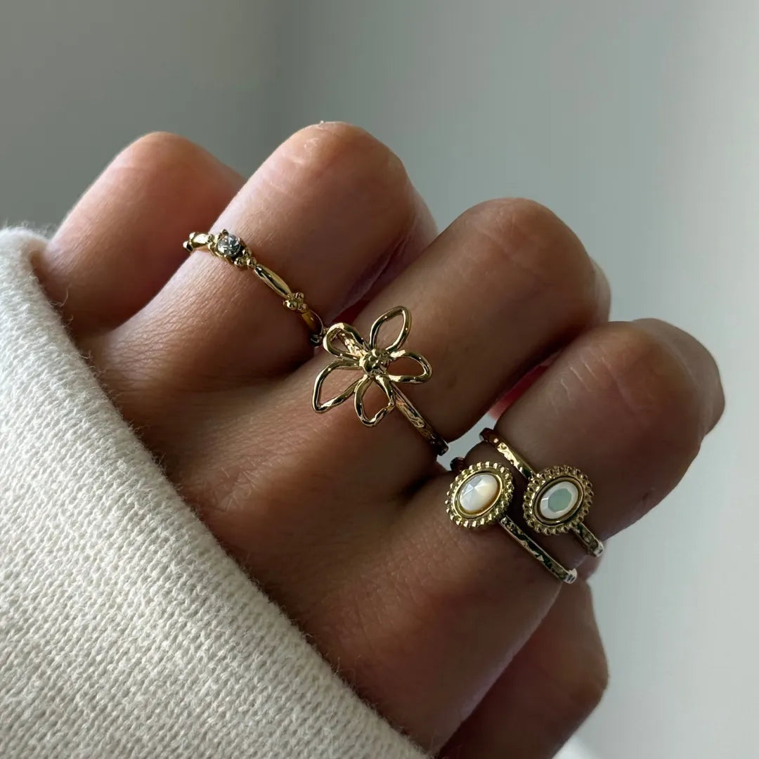 Bague ajustable en acier inoxydable doré, ornée d'une fleur ajourée délicate à l'effet martelé sur un doigt.