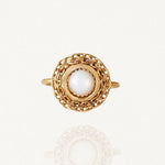 Bague dorée ronde avec une pierre blanche centrale (type nacre) entourée d'un motif maillons de chaîne ajouré sur fond blanc.