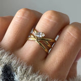 Bague multirang en acier inoxydable doré, entrelacée et ornée d'un zirconium ovale, portée sur un doigt.