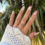 Bague triple rang en acier inoxydable dorée et texturée, portée sur une main aux ongles manucurés et pull blanc.