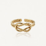 Bague ajustable en acier inoxydable dore avec un noeud central de brins tordus et lisses entrelaces.