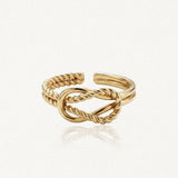 Bague ajustable en acier inoxydable dore avec un noeud central de brins tordus et lisses entrelaces.