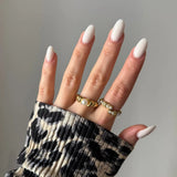 Main femme, ongles ovales blancs. Deux bagues dorées: une avec perle centrale, l'autre avec petites perles entrelacées. Manche léopard.