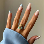 Main manucurée avec des ongles à pois bleus et blancs, portant trois bagues dorées empilées aux pierres variées.