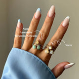 Main gauche portant 6 bagues en or avec pierres de nacre, amazonite et turquoise africaine. Manucure French bleue et pois.