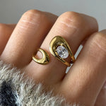 Main portant une bague ouverte en acier inoxydable doré, design double goutte avec un zirconium ovale brillant.