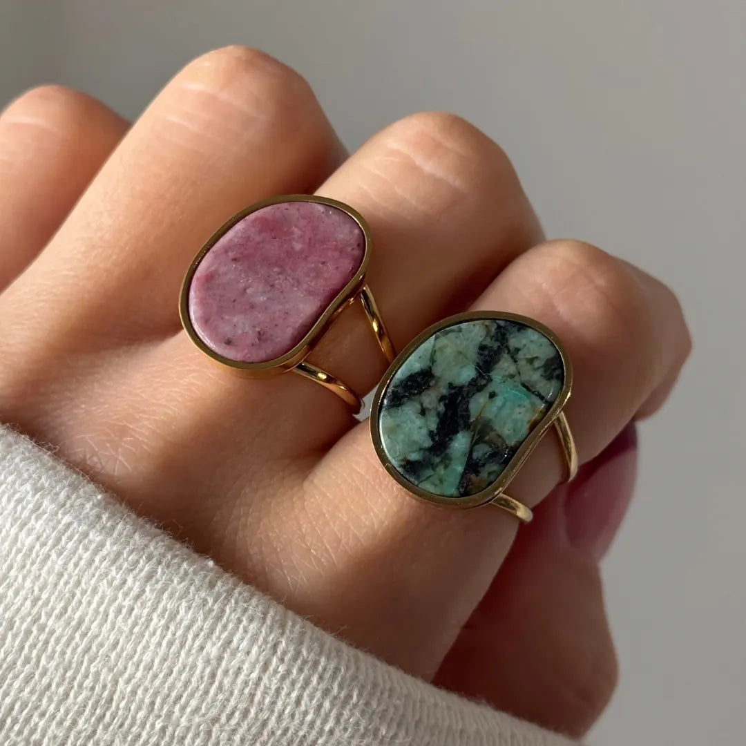 Deux bagues en acier inoxydable doré, une avec pierre naturelle rose, l'autre en Amazonite, sur une main.