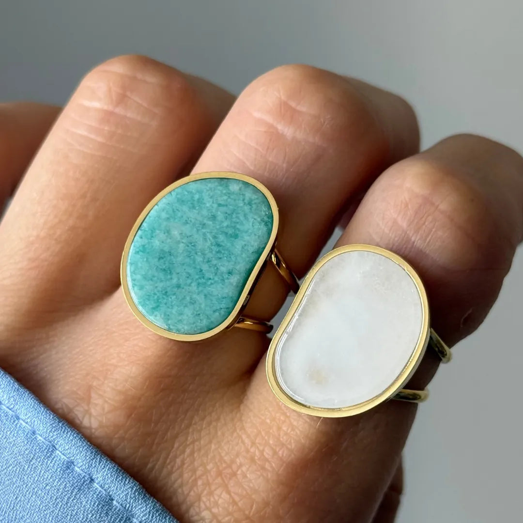 Main avec deux bagues dorées. L'une, sur l'index, a une pierre ovale irrégulière vert-turquoise. L'autre, sur le majeur, a