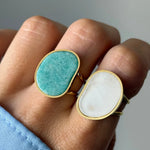 Main avec deux bagues dorées. L'une, sur l'index, a une pierre ovale irrégulière vert-turquoise. L'autre, sur le majeur, a