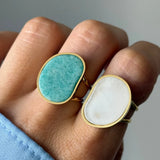 Main avec deux bagues dorées. L'une, sur l'index, a une pierre ovale irrégulière vert-turquoise. L'autre, sur le majeur, a