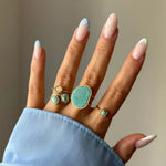 Main portant 5 bagues dorées aux pierres vert d'eau et jaune clair. Ongles manucurés avec motifs points blancs et bouts