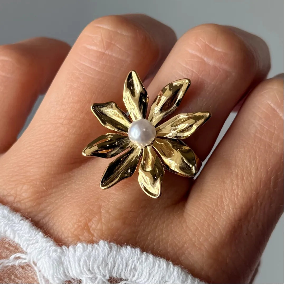Bague fleur en acier inoxydable doré, aux pétales texturés et ornée d'une perle blanche ronde au centre, portée au doigt.