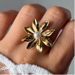 Bague fleur en acier inoxydable doré, aux pétales texturés et ornée d'une perle blanche ronde au centre, portée au doigt.