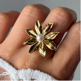 Bague fleur en acier inoxydable doré, aux pétales texturés et ornée d'une perle blanche ronde au centre, portée au doigt.
