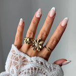 Bague fleur en acier inoxydable doré avec une perle blanche au centre, portée sur une main.