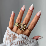 Bague fleur en acier inoxydable doré avec une perle blanche au centre, portée sur une main.