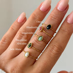 Main portant cinq bagues en acier inoxydable dore avec des pierres ovales : Onyx, Rhodonite, Amazonite, Turquoise Africaine,