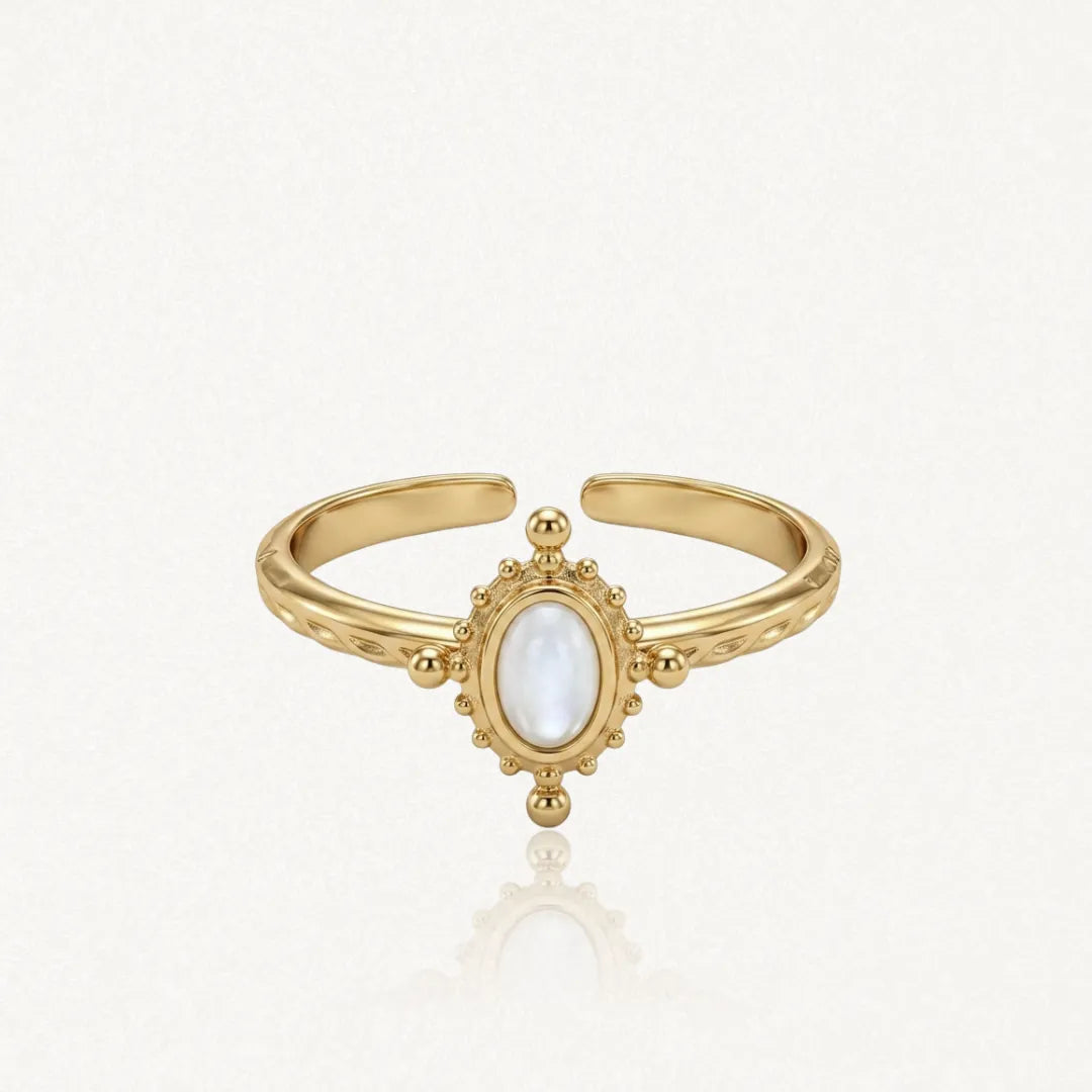 Bague ajustable en acier inoxydable doré, avec nacre ovale au centre, encadrée de motifs perlés. Bande gravée.