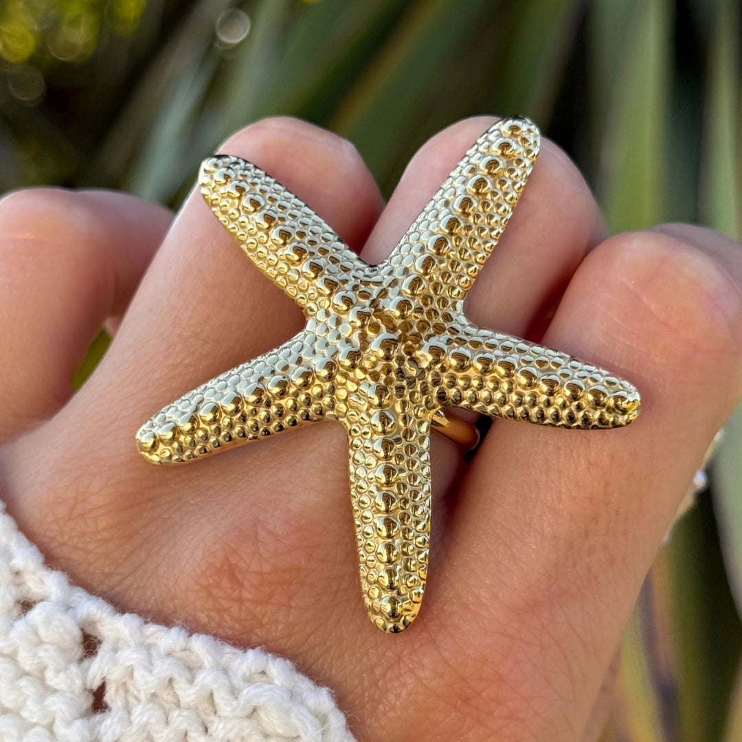 Grande bague étoile de mer dorée en acier inoxydable texturé portée sur une main.