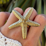 Grande bague étoile de mer dorée en acier inoxydable texturé portée sur une main.