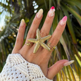 Bague en acier inoxydable dorée, grande étoile de mer texturée et petites étoiles. Bijou thème marin sur main de femme.