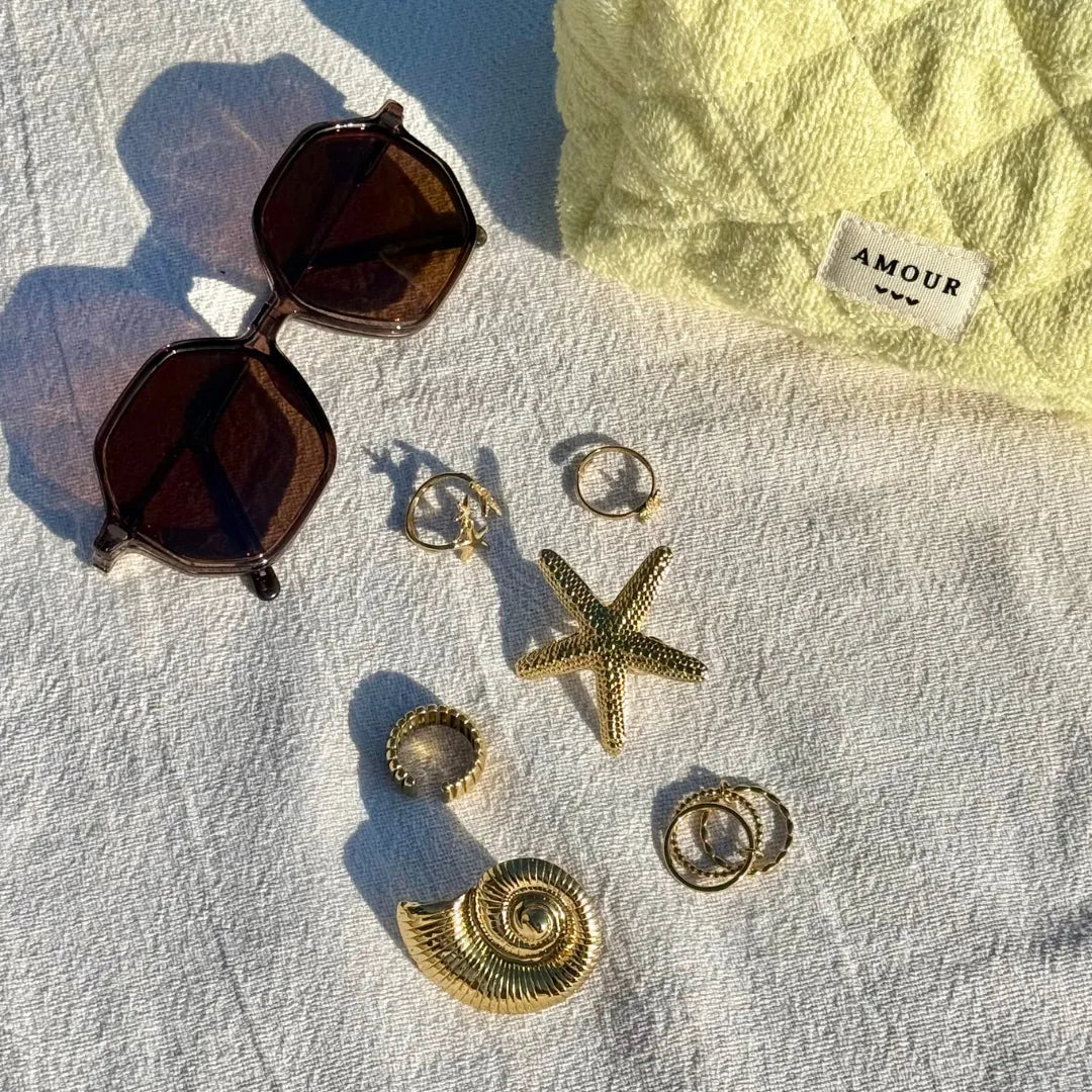 Bague étoile de mer texturée, d'autres bagues et un coquillage, tous en acier inoxydable doré, avec lunettes sur tissu blanc.
