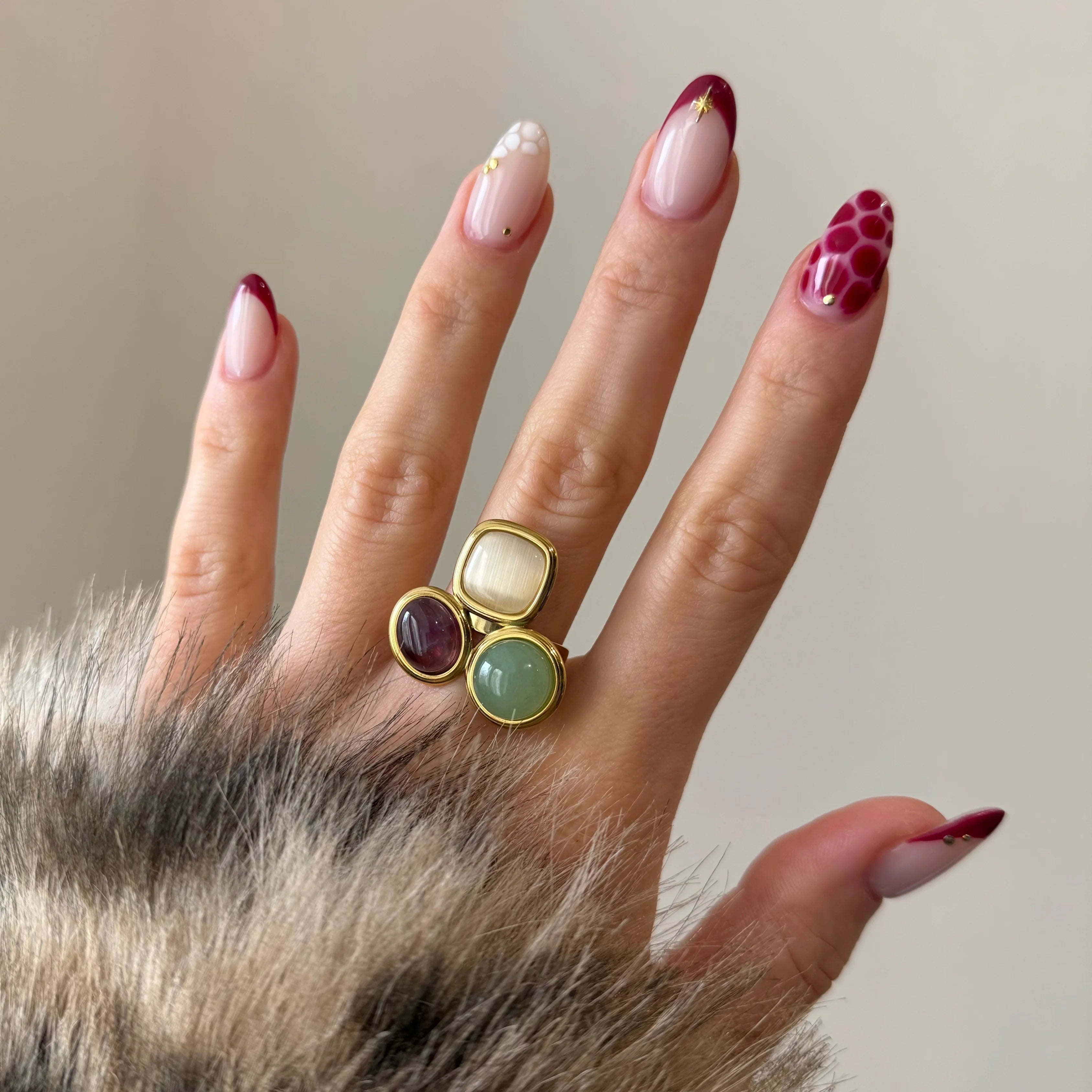 Bague originale multicolore portée sur une main manucurée, accessoirisant une tenue avec fausse fourrure.