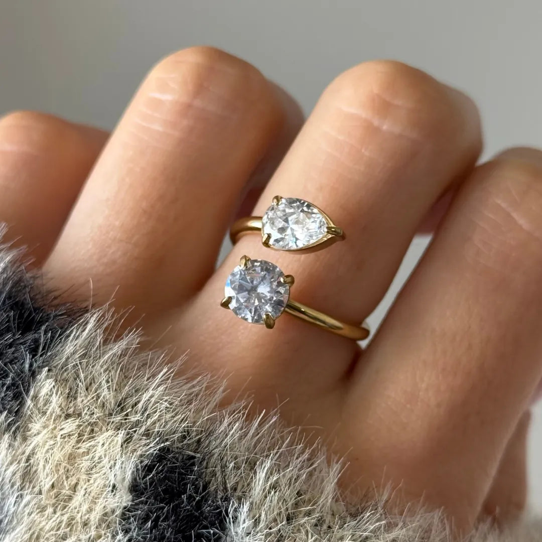 Bague toi et moi en acier inoxydable doré, avec un zirconium poire et un zirconium rond, portée au doigt.