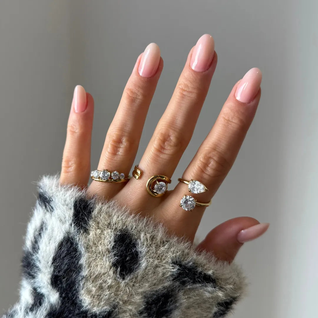 Main aux ongles roses poudrés, manche de pull animal. Elle porte 3 bagues en acier inoxydable doré à zircons, dont une toi et