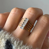 Bague manchette multirangs en acier inoxydable doré, ornée de six pierres baguette en Zirconium, portée au doigt.