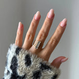 Bague manchette multirangs en acier inoxydable doré avec six zircons baguettes sur une main aux ongles rosés et pull léopard.