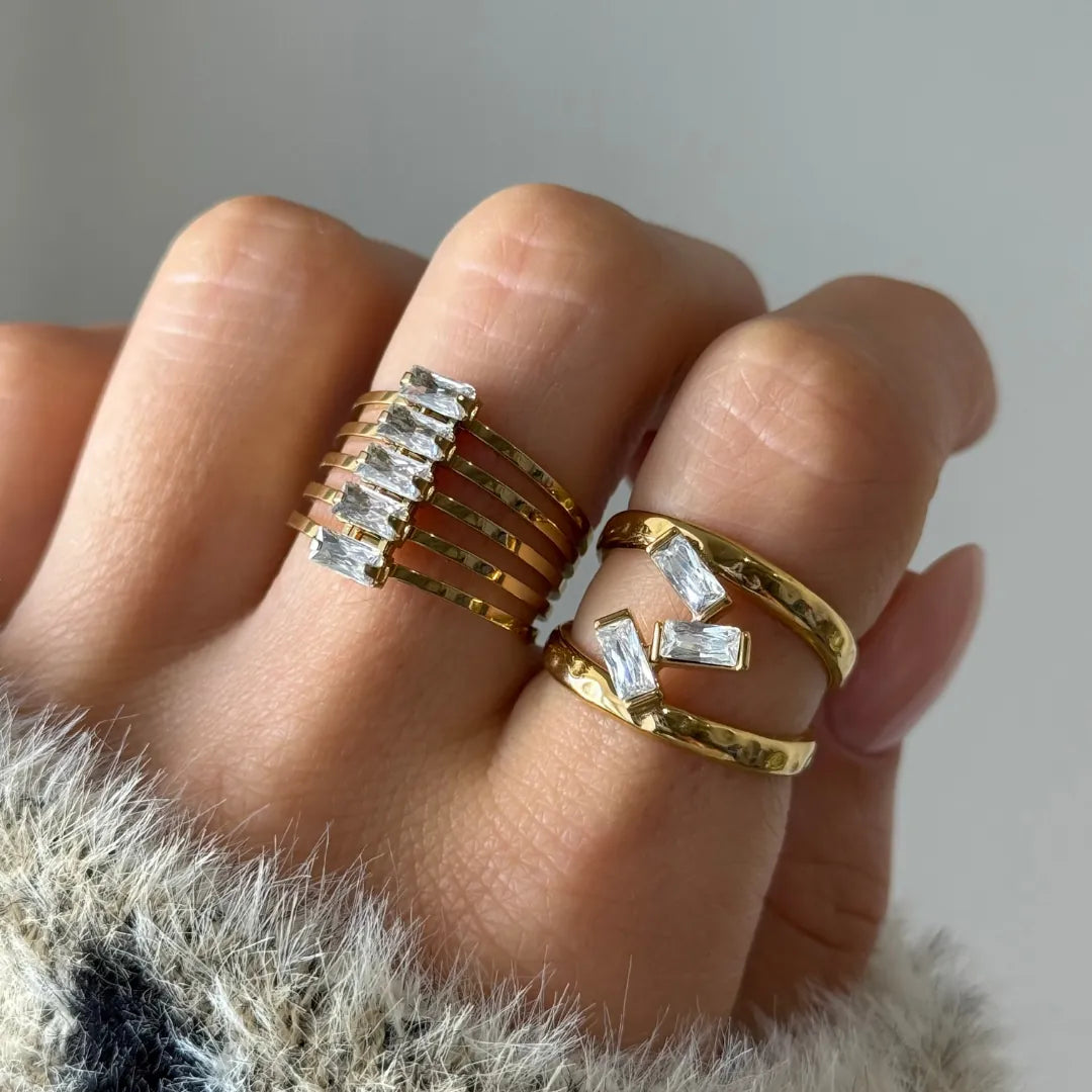 Bague manchette multirangs en acier inoxydable doré, ornée de six pierres baguette en Zirconium, portée sur un doigt.
