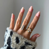 Main de femme avec bague manchette multirangs en acier inoxydable doré, six zirconiums baguette et une bague dorée.