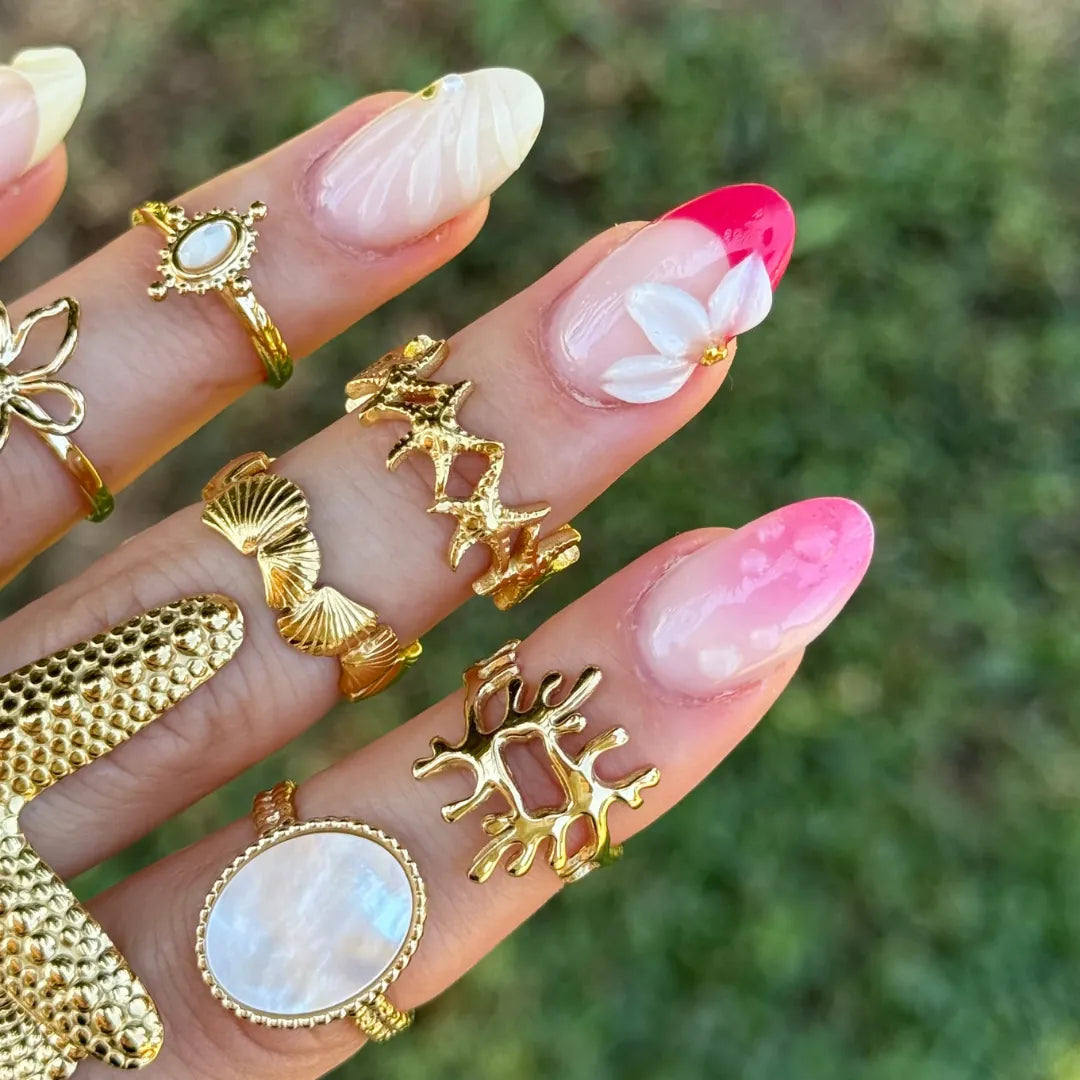Main avec plusieurs bagues en acier inoxydable doré, dont une bague étoiles de mer et des bagues avec de la nacre, sur fond