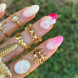 Main avec plusieurs bagues en acier inoxydable doré, dont une bague étoiles de mer et des bagues avec de la nacre, sur fond