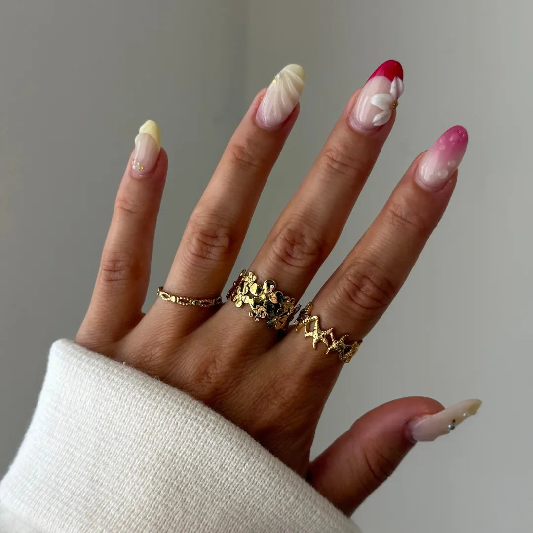 Main portant une bague en acier inoxydable doré à motifs étoiles de mer, un pull blanc et des ongles décorés.