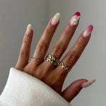 Main portant une bague en acier inoxydable doré à motifs étoiles de mer, un pull blanc et des ongles décorés.