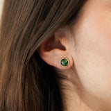 Femme portant la puce d'oreille ronde verte, bijou discret et élégant idéal pour une touche de couleur au quotidien.