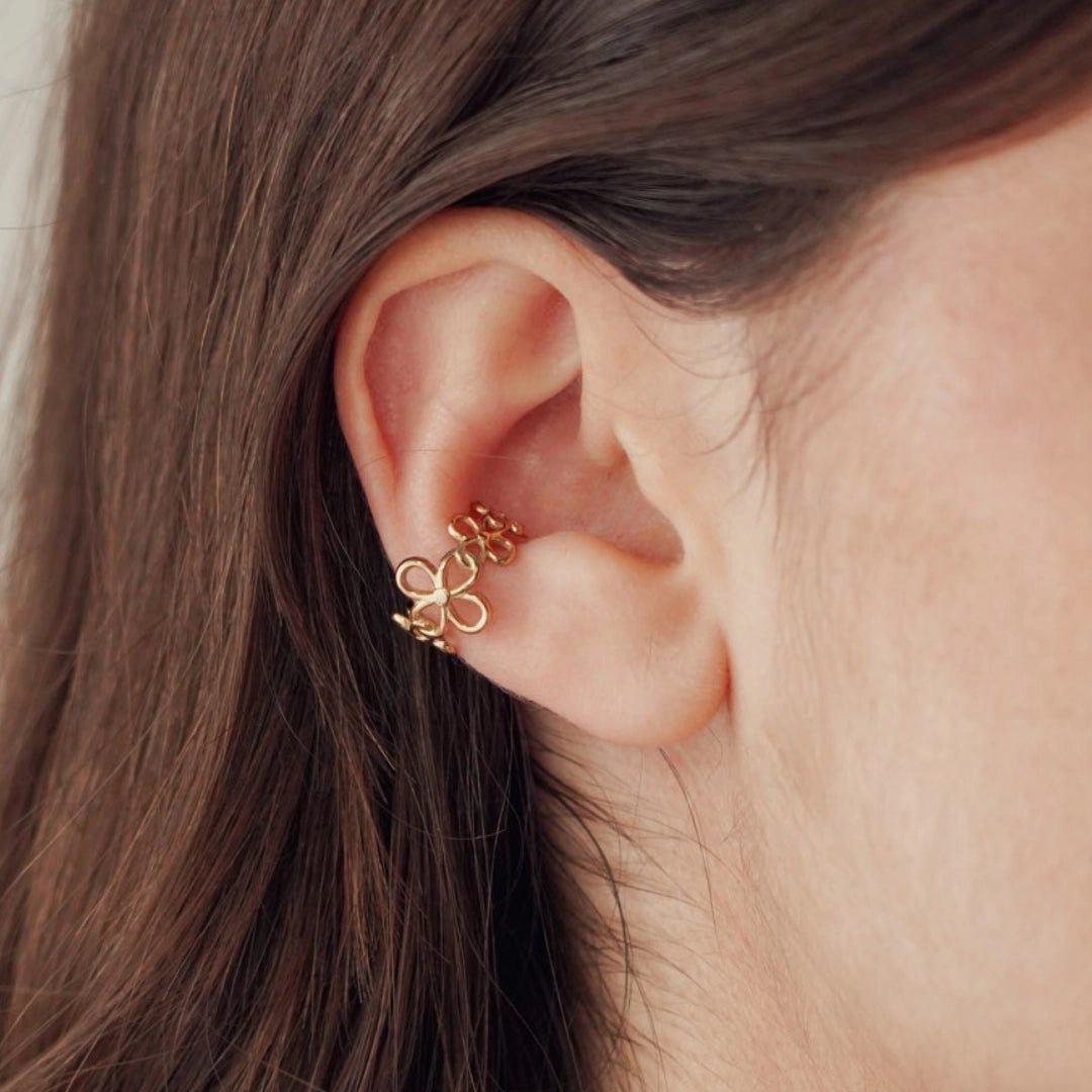 Boucles d'oreilles en acier inoxydable doré, motif 3 fleurs délicates, sur le cartilage d'une oreille.