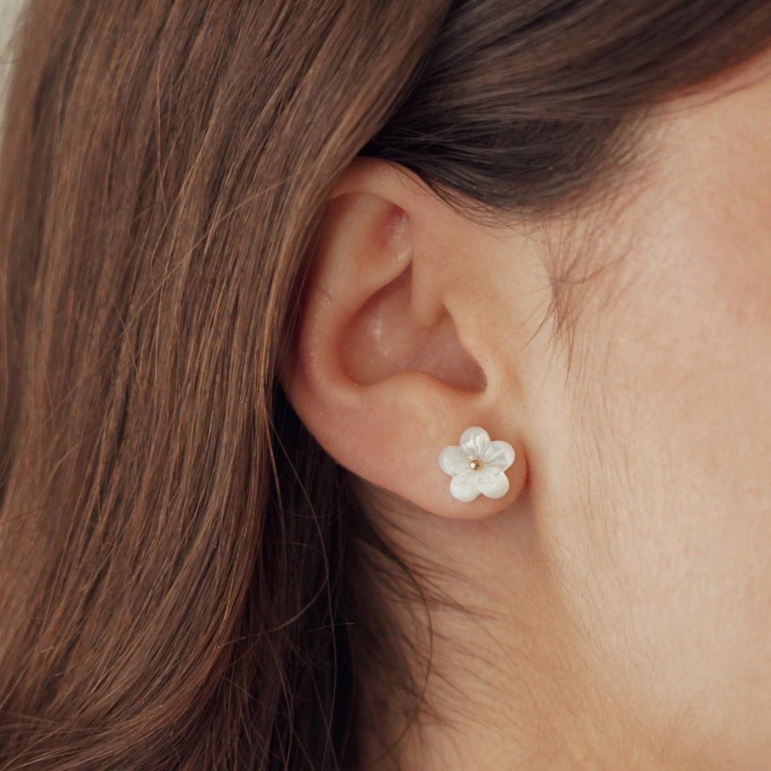 Boucles d'oreilles puces fleur blanche en acier inoxydable avec cœur doré, portées sur une oreille.