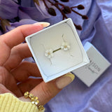 Boucles d'oreilles en acier inoxydable, motif fleur blanche nacrée avec centre doré, dans un écrin blanc.