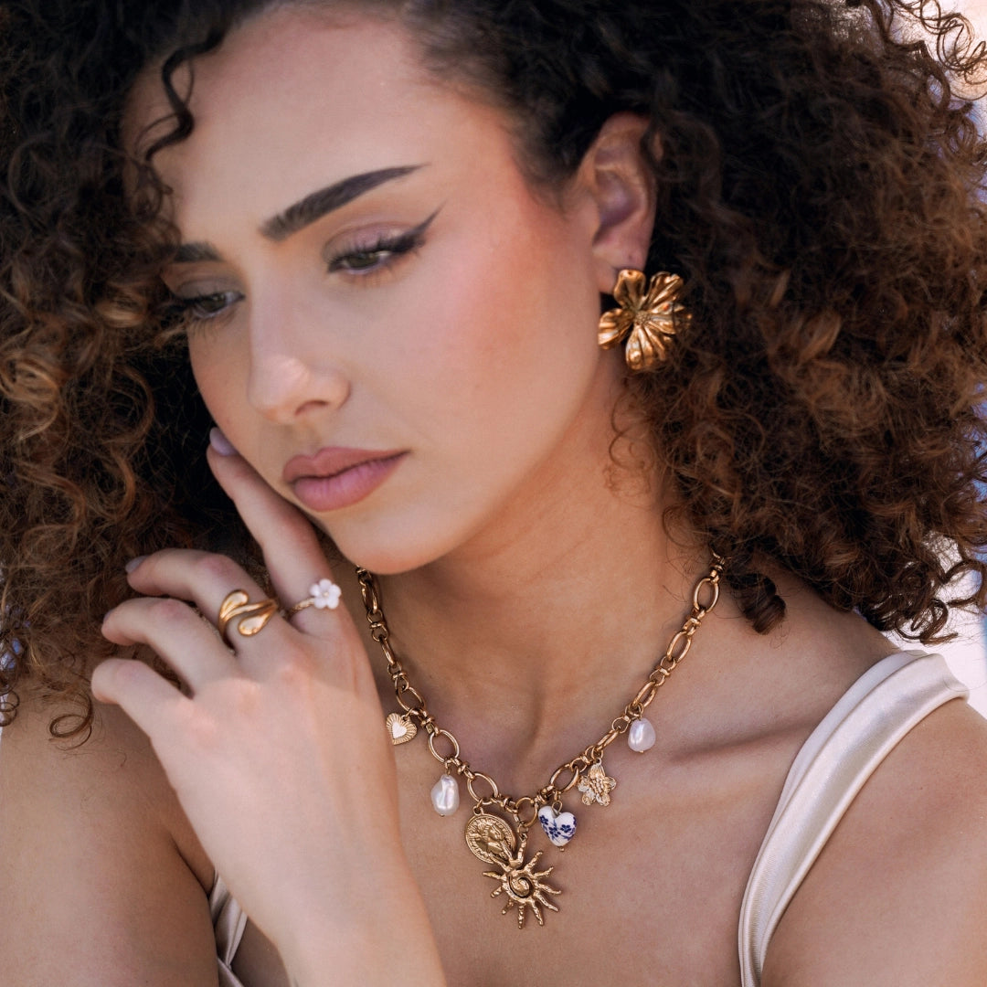 Boucles d'oreilles fleur dorée texturée en acier inoxydable, portées par une femme aux cheveux bouclés.